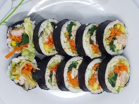 Kimbap rolls arranged diagonally on a white plate with a minimal and bright background.