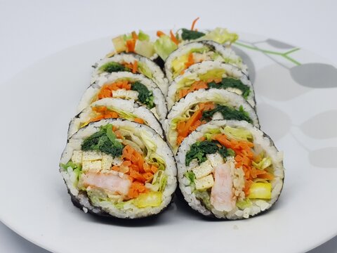 Close-up photo of sliced kimbap rolls showing texture and colorful vegetable fillings on white plate.