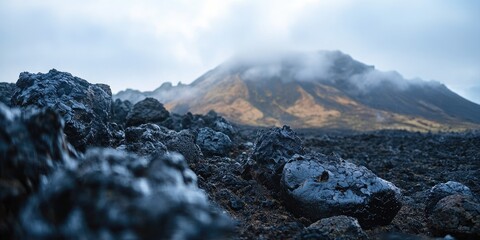 A rugged, rocky landscape with a mountain in the background, covered in clouds and fog, with a rocky foreground and a cloudy sky.