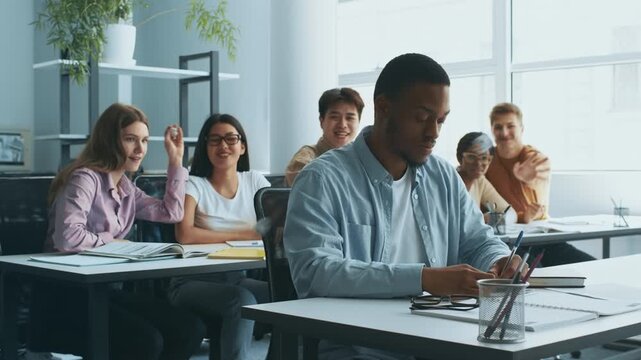 Diverse group of students bullying their classmate African American guy sitting in front, classroom interior