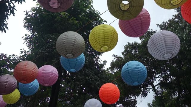 Many beautiful colorful Chinese lanterns hang in the wind in the garden.