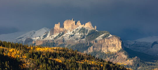 This stunning autumn mountain panorama features accent light on one of Colorado's most unique rock formations, the Castles, and golden aspen trees as dark storm clouds create a contrasting background. © Nick Monitello