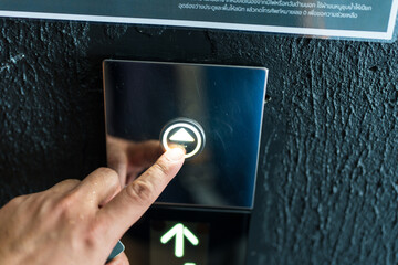 A hand presses a button on an elevator panel
