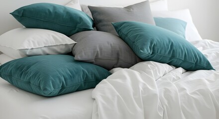 Pillows in various teal, grey and white hues are piled casually on a white sheeted bed