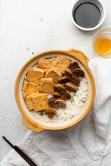 Overhead view vegan claypot rice with pan fried tofu, mushrooms and scallions, top view of crispy rice in a donabe on a marble countertop