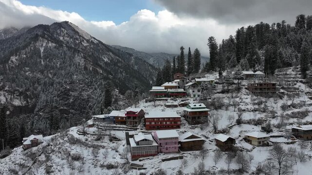 A breathtaking aerial drone shot captures a remote mountain village in the Himalayas, completely covered in fresh, glistening snow. A stunning winter landscape for travel or nature projects.