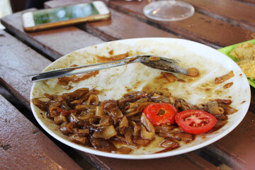 A white plate with leftover fried noodles and sliced tomatoes on a wooden table