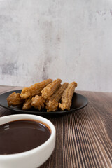 Approach to table with some churros on a plate, there is chocolate to accompany