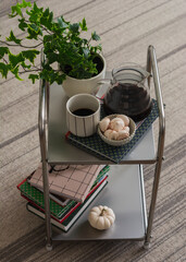 A glass of coffee, a pot of coffee, meringue in a bowl, a book, a pet flower on a metal table in the living room. Coffee break