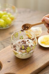 Adding Cereal to Yogurt for a Healthy Breakfast, with granola and yogurt in glass bowl on wooden table, stock photo
