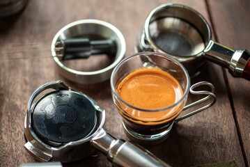Espresso Tools: Professional Portafilter and Glass Cup with Rich Crema on Rustic Wooden Table Espresso Perfection: Dark Roast Coffee with Crema, Portafilter, and Chrome Machine Parts on Wood