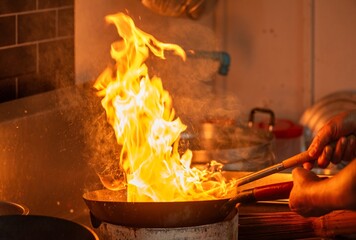 Man is cooking food in a kitchen with a lot of smoke and fire