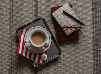 A cup of tea with milk, meringue on a metal tray, notebooks, glasses on the carpet, top view
