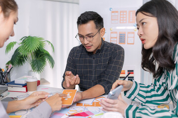 A group of UX/UI designers brainstorming creative ideas together, discussing color palettes and layout concepts for a new mobile application interface in a modern design office.