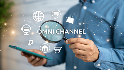 Fototapeta premium A man is holding a magnifying glass over the words omni channel with icons of a globe, credit card, shopping bag, bank, music, house, and shopping cart