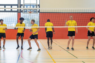 Diverse male teammates in yellow shirts practicing blocking drills on court with net, hoop