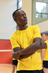 African american male player crossing arms by volleyball net in gym wearing yellow jersey shorts