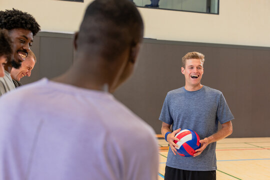 Male volleyball team watching coach holding volleyball showing serve on court, copy space - Powered by Adobe