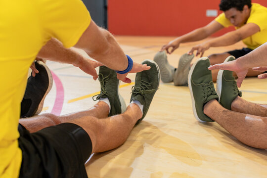 Diverse male teammates in yellow shirts, black shorts stretching on court floor touching shoes