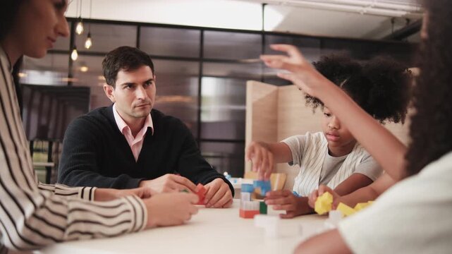 Group of multiracial students and teachers playing fun mathematical puzzle game on tables together, creatively learning in primary class, kids challenge for wisdom at elementary international school.