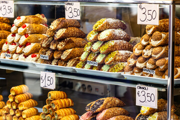 A tempting window display of stacked Sicilian Cannoli pastries in Venice, featuring classic, pistachio, and amaretto flavors, with handwritten price tags showcasing Italian street food.

