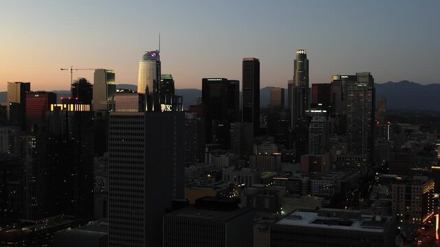 Cinematic aerial of Downtown Los Angeles while the sun sets for the day, reflecting beams of light throughout the skyline between the buildings 