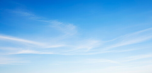 Blue sky with thin white clouds forming delicate wisps across the atmosphere, capturing the calmness of a clear midday with bright natural sunlight.
