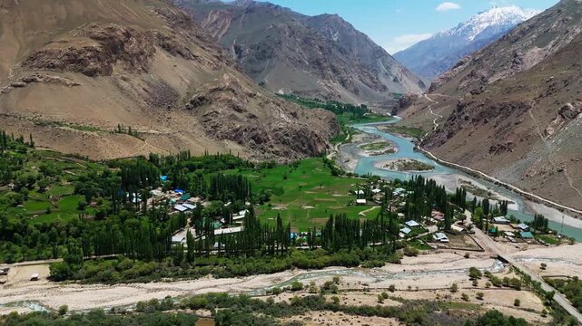 Aerial view of the Wakhan Valley, showing the river that forms the natural border between Tajikistan and Afghanistan, surrounded by dramatic mountains and agricultural green fields and villages 