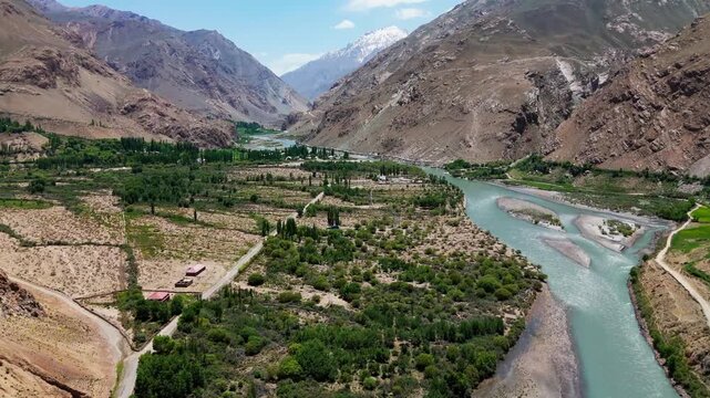 Aerial view of the Wakhan Valley, showing the river that forms the natural border between Tajikistan and Afghanistan, surrounded by dramatic mountains and green fields