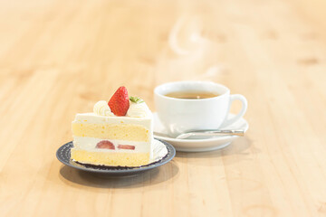 Delicious strawberry cake and steaming cup of tea on a wooden table in a cozy cafe