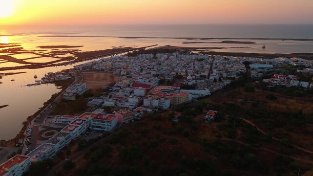 aerial shot above Fustea fishing village at sunrise near Ria Formosa natural park in Algarve region with the village in the foreground and the salt pans in the background, Portugal