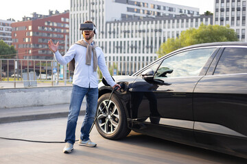 A man wearing a VR headset is charging his electric vehicle in an urban setting, experiencing virtual reality.