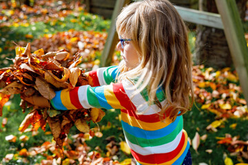 Autumn portrait of little preschool girl in autumn park on warm october day playing and throwing...