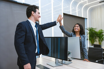 Two business people celebrate a successful collaboration with high fives in a office, conveying teamwork and success.