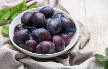 Fresh ripe plums in white bowl on table