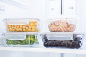 Berries, vegetables, and tuna in glass containers in the refrigerator, food storage concept.