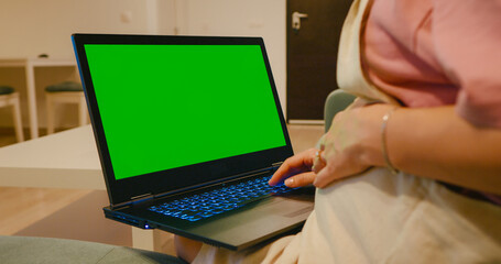Pregnant business woman typing on chroma key laptop indoors. Closeup expectant mother working computer with green screen at home.