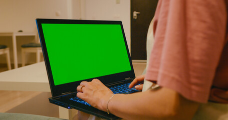 Pregnant woman typing on chroma key laptop indoors. Closeup expectant mother working computer with green screen at home.