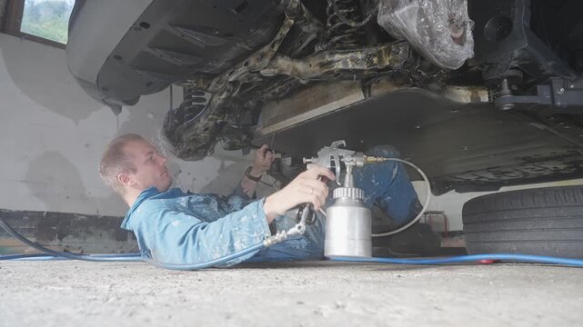 Man spraying ecofriendly lanolin rustproofing on car undercarriage to prevent corrosion, coating parts of suspension components