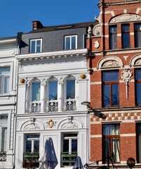 Architectural contrast: a neoclassical white stucco facade with columns next to an ornate red brick Neo-Renaissance building in Antwerp, Belgium