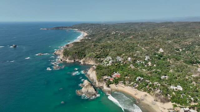 Aerial orbit around Mazunte on Mexico&rsquo;s Pacific coast, revealing green hilltops, rocky cliffs and sandy coves. Clear day with expansive coastal relief; Punta Cometa visible in the distance.