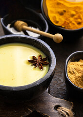 cup of golden milk, the traditional Ayurvedic turmeric-infused drink, served in a matte black mug, surrounded by fresh spices and roots on a textured concrete surface