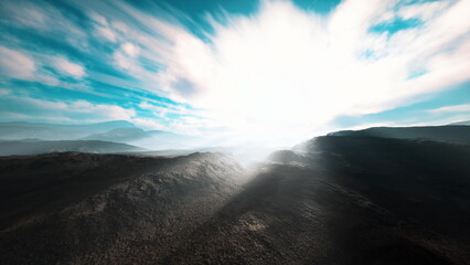 Sunlight bursts forth over distant mountains, casting warm rays onto the rugged terrain. Clouds drift softly in the bright blue sky, creating a serene and majestic atmosphere. © icetray
