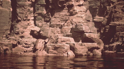 Calm waters reflect unique rock formations at sunset, creating a serene atmosphere. The warm colors illuminate the cliffs, highlighting their texture and beauty.