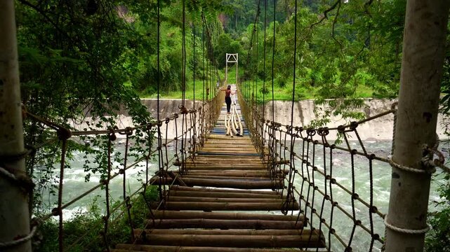 Long wobbly suspension bridge on ropes and cables made of bamboo over a strong mountain river with clear water in the tropics