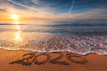 Ocean Beach Sunrise with 2026 Happy New Year Text Written in Sea Sand and Splashing Ocean Waves on the Shore concept for beautiful new beginning