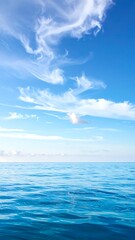 Obraz premium Tranquil ocean surface under a clear, azure sky with wispy clouds. The horizon is distinct