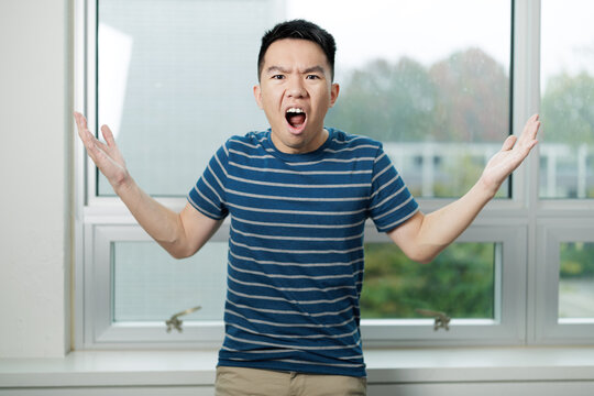 Young man standing indoors with arms out and puzzled expression, symbolizing confusion or uncertainty. Suitable for concepts like misunderstanding, frustration, or questioning.