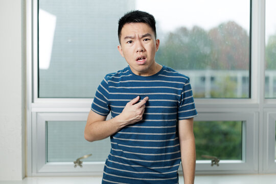 Young man in striped shirt pointing at his chest with a confused and surprised expression. Represents disbelief, self doubt, or questioning responsibility.
