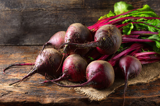 Fresh vibrant beets with green tops on rustic wood, healthy organic farm produce still life.